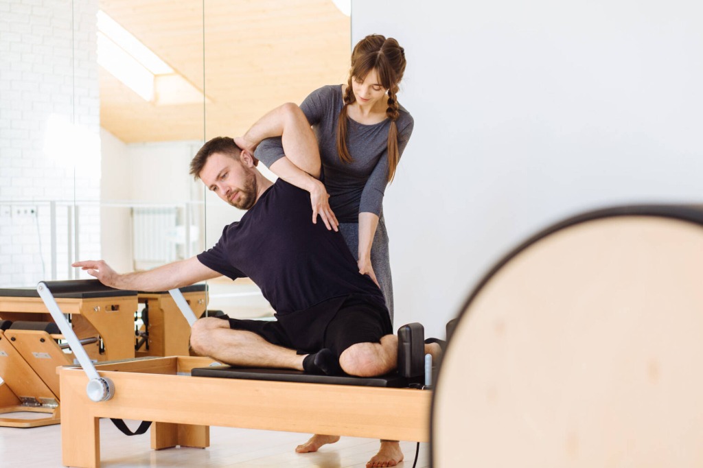 Fisioterapeuta guiando y ajustando la postura en máquina de Pilates Reformer